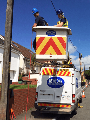 Small image of Newconn workers in cherry picker and newconn vehicle next to a woodpole line.