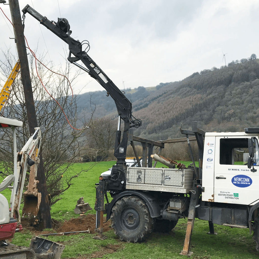 Wooden pole being installed by vehicle and crane on site in wales